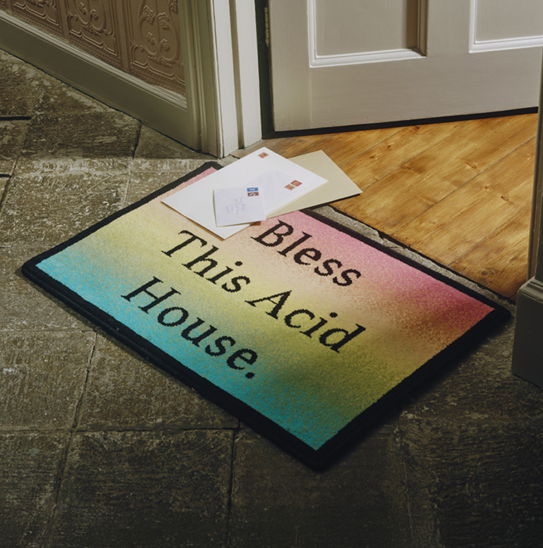 Doormat with 'Bless This Acid House' text on a wooden floor.